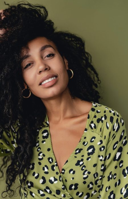 attractive black african american woman posing in stylish green leopard printed dress isolated on green studio background, summer fashion trend, happy smiling curly hair