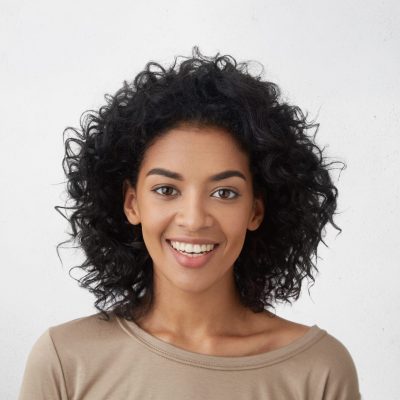 Close up shot of pretty girl with perfect teeth and dark clean skin having rest indoors, smiling happily after received good positive news. Beautiful young woman with Afro hairstyle relaxing at home