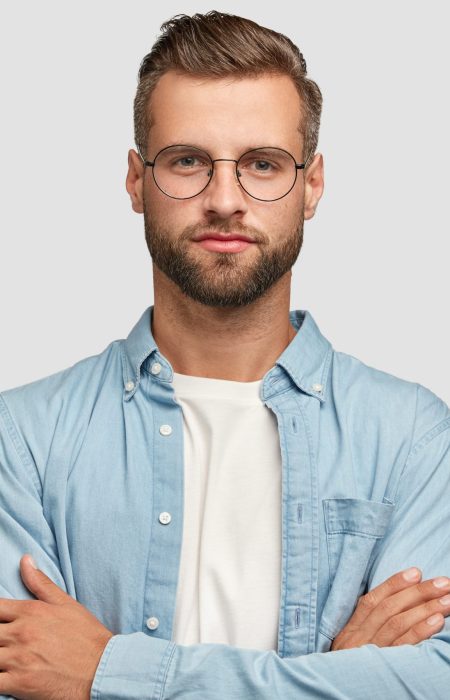 Horizontal shot of handsome self confident businessman or designer, stands crossed hands against white background, wears casual shirt, poses against white background. People and lifestyle concept