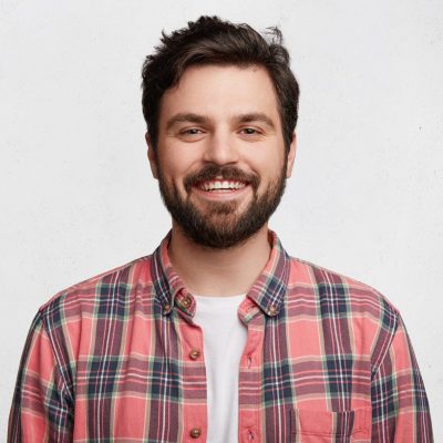 Smiling bearded young male model rejoices coming weekends, dressed casually, isolated over white background. Positive pleased student being in good mood after successfully passed exams at college